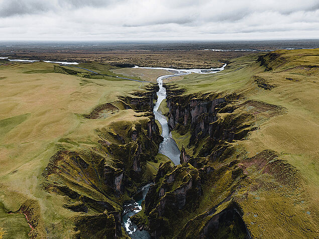 Tiefes Tal in Island, unten ein Fluss, am Horizont Wolken 